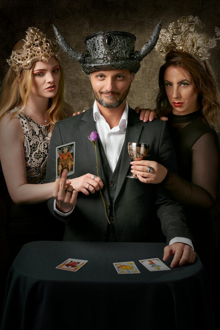 A stylish group poses glamorously indoors, each holding a tarot card, exuding royalty and mystery.
