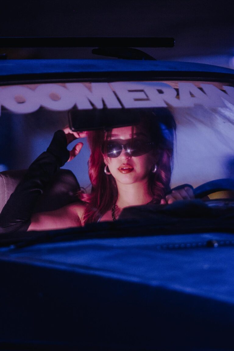 Chic woman with red hair in a car, wearing sunglasses and gloves, creating a moody night atmosphere.