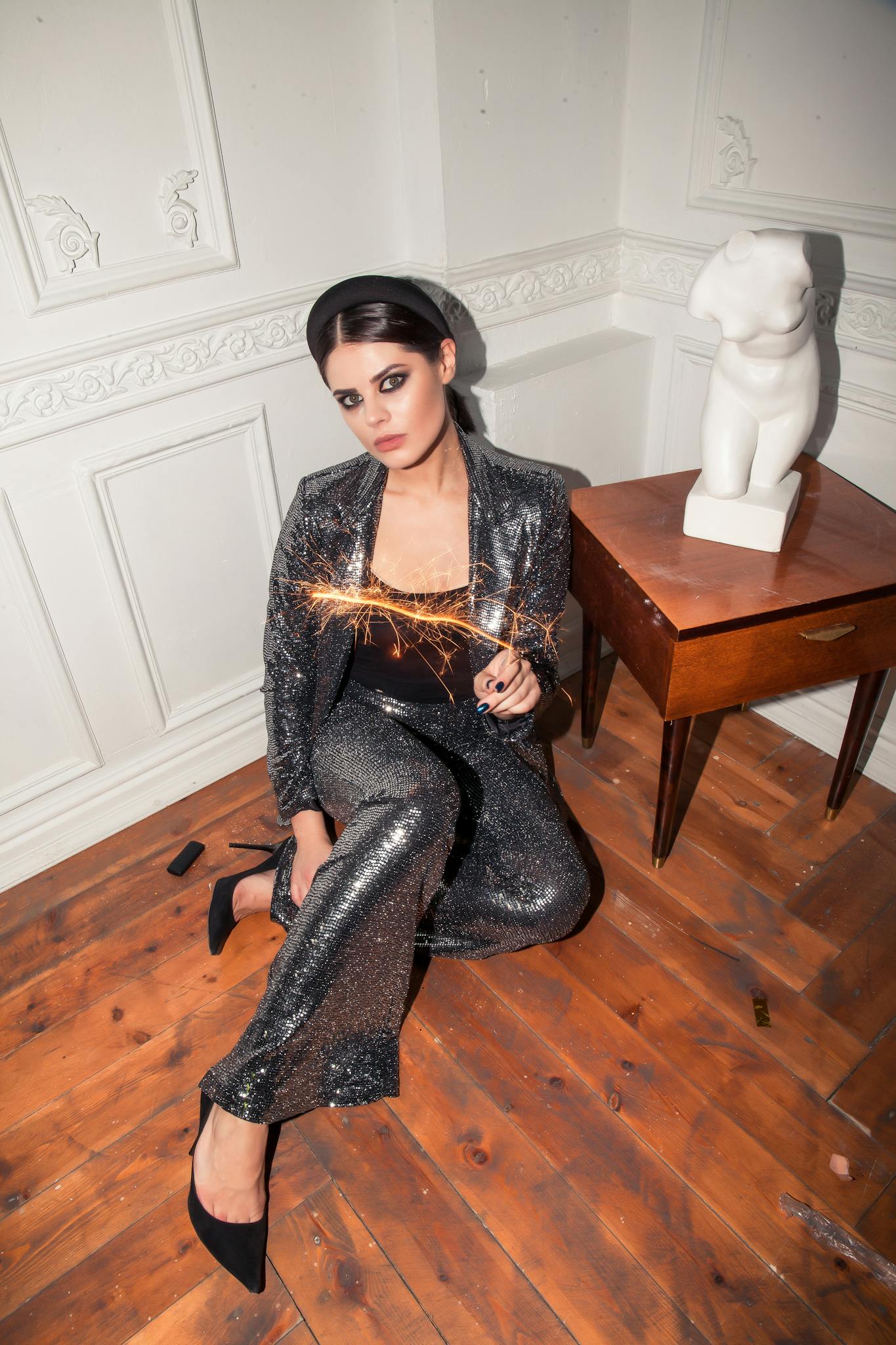 Elegant woman in a sparkling outfit holding sparklers, celebrating New Year's Eve indoors.